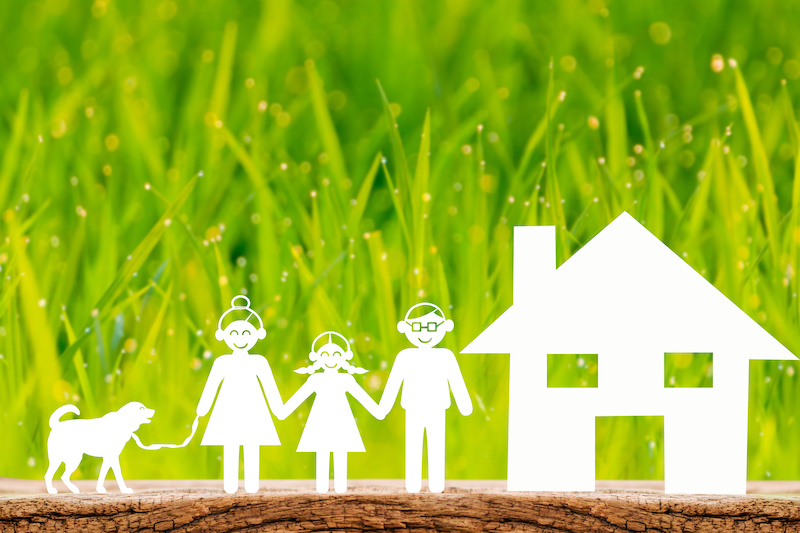 Home and happy family and dog of paper cut put on the wood on green grass background, Saving money for house or real estate owner in the future concept.