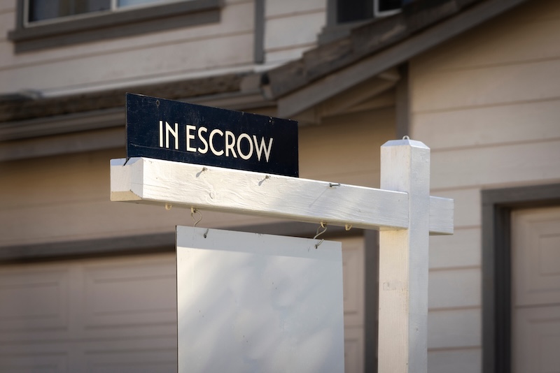 A sign stating In Escrow with a house in the background