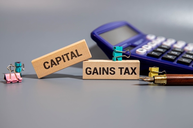 CAPITAL GAINS TAX word. Copy space. Concept word CAPITAL GAINS TAX on wooden blocks with diagram chart and office stuffs on the background. Business and financial concept.