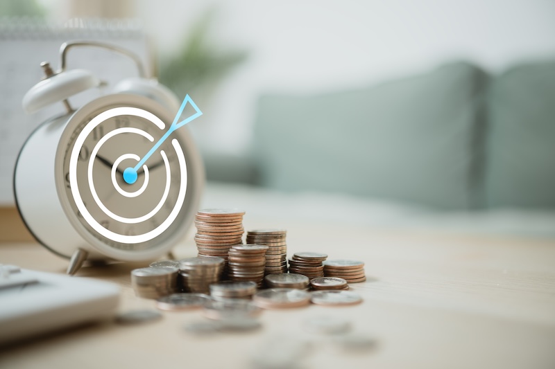 Tracking savings goals with coins, an alarm clock, and target icon symbolizes financial planning, budgeting, and steady progress toward future security.